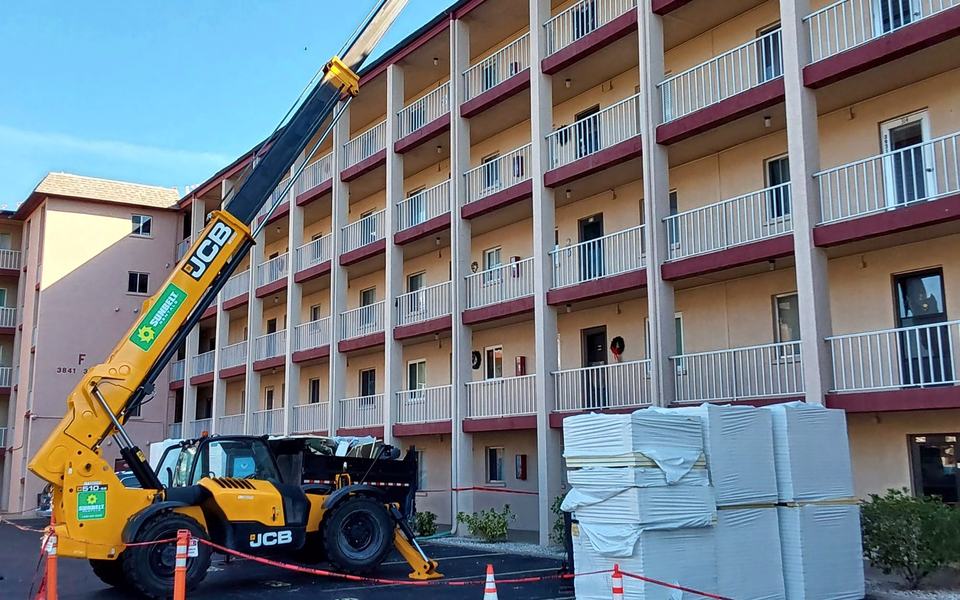 Telehandler lifting roofing materials beside a multi-story building